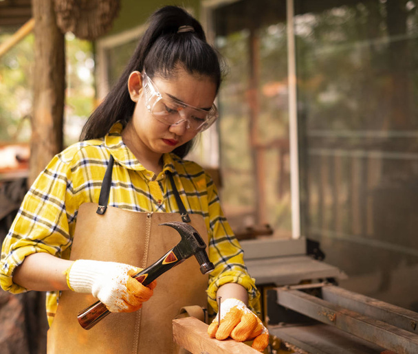 女性ビルダーを着て立っているチェック シャツ木製イノシシに釘を打って建設現場の労働者 - 写真・画像