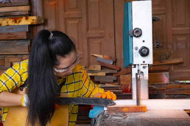 Femmes debout est l'artisanat de travail du bois coupé sur un banc de travail avec scies à ruban outils électriques à la machine charpentier dans l'atelier, travailleurs planches à scier de avec scierie transformation du bois une entreprise familiale
 - Photo, image