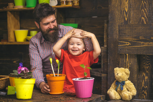 Family day. Greenhouse. bearded man and little boy child love nature. Flower care watering. Soil fertilizers. happy gardeners with spring flowers. Father and son. Fathers day. Look at it - Photo, image