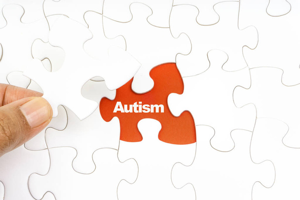 Hand holding piece of jigsaw puzzle with word AUTISM. Selective focus - Фото, зображення