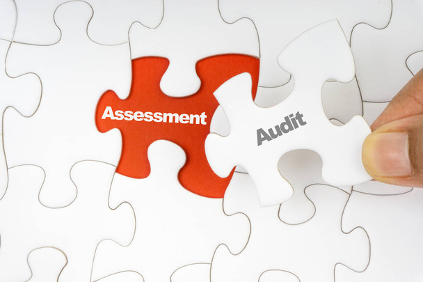 Hand holding piece of jigsaw puzzle with word AUDIT ASSESSMENT. Selective focus - Photo, Image