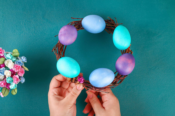 Diy Easter wreath of twigs, painted eggs and artificial flowers on a green background. - Foto, afbeelding