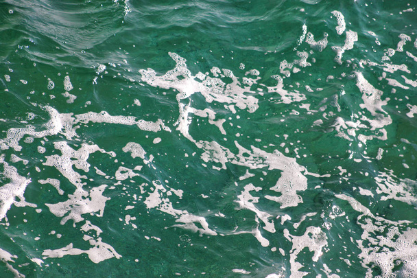 Turquoise groen zeewater met schuim van de zee als achtergrond, close-up. Oppervlakte van zee met golven, splash, schuim en bubbels, blauwe abstracte textuur en behang. Mooie groene golven met een heleboel schuim van de zee. - Foto, afbeelding