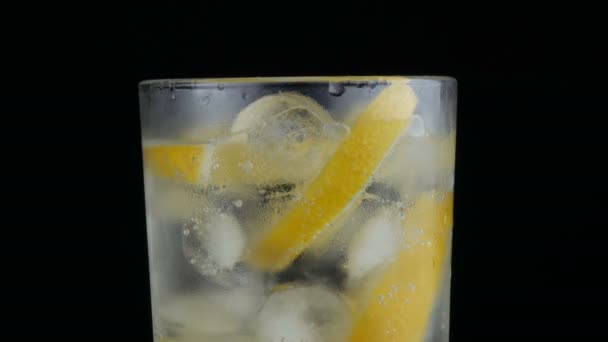 Нарізаний лимон у довгій склянці з кубиками льоду та холодною содовою на чорному тлі крупним планом. Освіжаючі бульбашки лимонаду
. - Кадри, відео