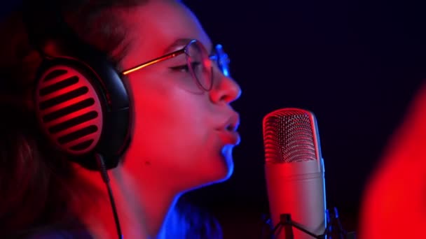 Una joven guapa con gafas y auriculares cantando en el estudio
 - Metraje, vídeo