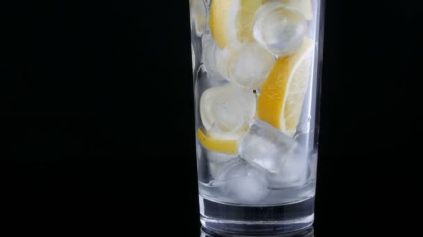 Long glass with lemon slices and ice cubes on a black background. - Footage, Video