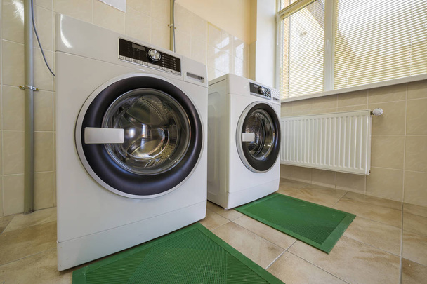 Современные новые промышленные стиральные машины в чистой кафельной ванной комнате o
 - Фото, изображение