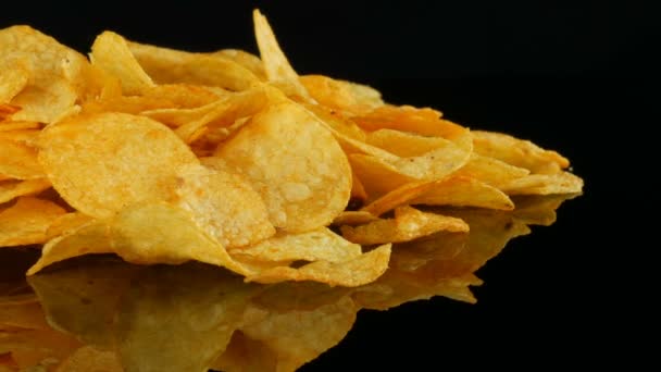 Chipsy ziemniaczane leżą na powierzchni lustra losowo rozrzuconych na czarnym tle. Szkodliwa żywność, Fast food - Materiał filmowy, wideo