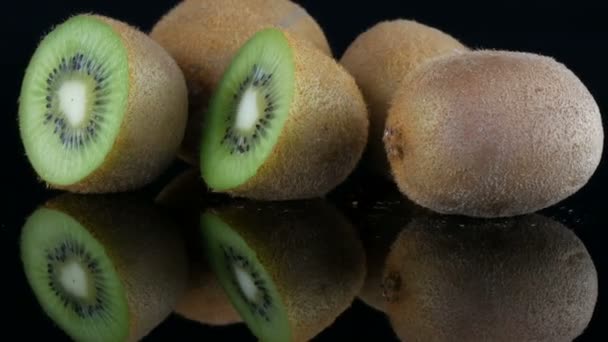 Vista elegante de la fruta madura en rodajas y kiwi entero rotado en una superficie de espejo sobre fondo negro en el estudio
 - Metraje, vídeo