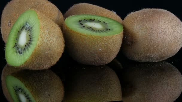 Vista elegante de la fruta madura en rodajas y kiwi entero rotado en una superficie de espejo sobre fondo negro en el estudio
 - Metraje, vídeo