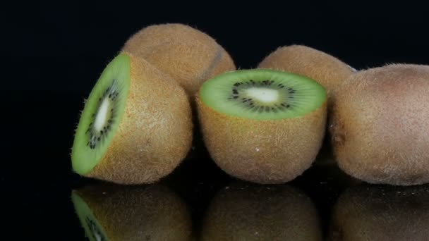 stilvolle Ansicht reifer geschnittener und ganzer Kiwi-Früchte auf Spiegelfläche auf schwarzem Hintergrund im Studio - Filmmaterial, Video