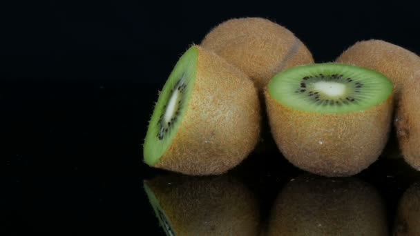 Vista elegante de la fruta madura en rodajas y kiwi entero en una superficie de espejo sobre fondo negro en el estudio
 - Metraje, vídeo
