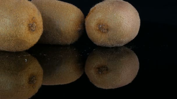 Female hands put ripe cut fruit next to whole kiwi on the mirror surface on a black background in studio - Footage, Video