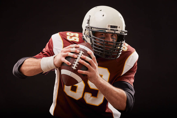 Retrato de jogador de futebol americano segurando uma bola com ambas as mãos
 - Foto, Imagem