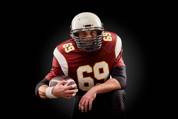 Πορτρέτο του αμερικανικού ποδοσφαίρου παίκτης που κρατάει μια μπάλα με τα δύο του χέρια - Φωτογραφία, εικόνα