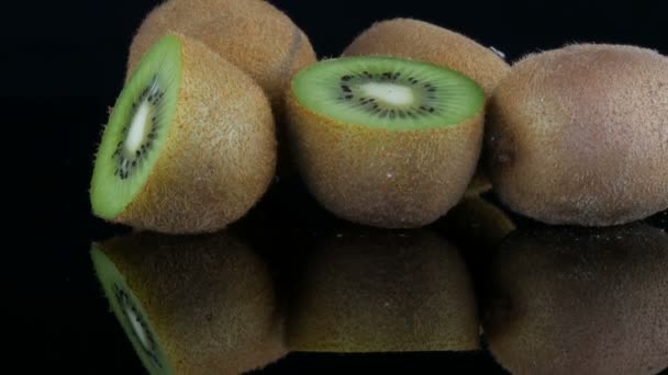 Stijlvolle kijk op rijp gesneden en hele Kiwifruit op een spiegeloppervlak op zwarte achtergrond in de Studio - Video