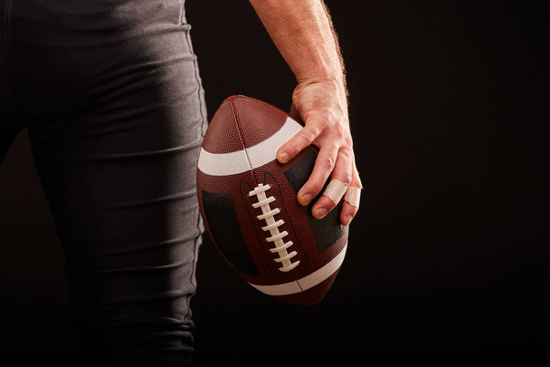 Mid section of American football player with ball against black, copy space, back view - Fotografie, Obrázek