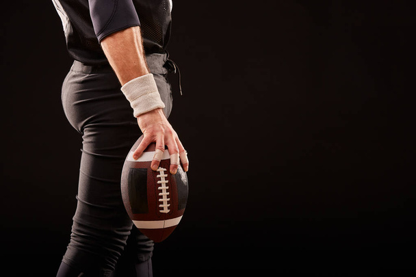 Mid sectie van American football-speler met bal tegen zwart, kopie ruimte, zijkant - Foto, afbeelding