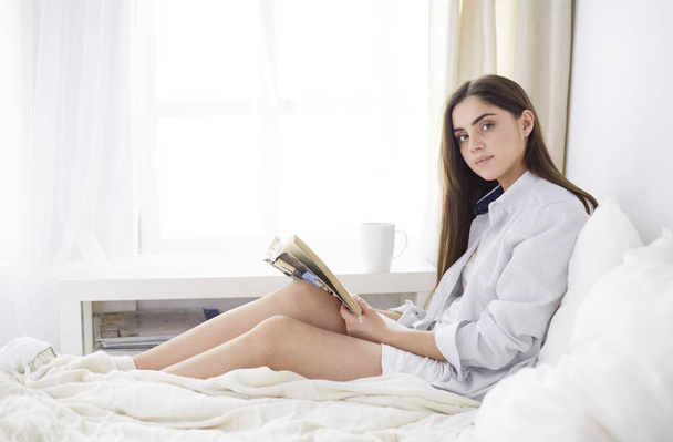 Portrait of woman using tablet and drinking coffee while sitting on the bed in the morning - Foto, Imagen
