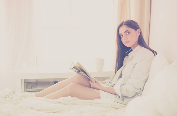 Portrait of woman using tablet and drinking coffee while sitting on the bed in the morning - Foto, afbeelding