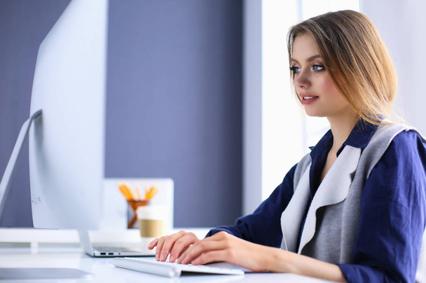 Young confident businesswoman working at office desk and typing with a laptop - Fotó, kép