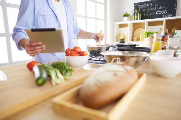 Man following recipe on digital tablet and cooking tasty and healthy food in kitchen at home - Photo, Image