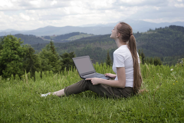 Bella ragazza sognante con un computer portatile seduto su erba verde su uno sfondo di montagne
 - Foto, immagini