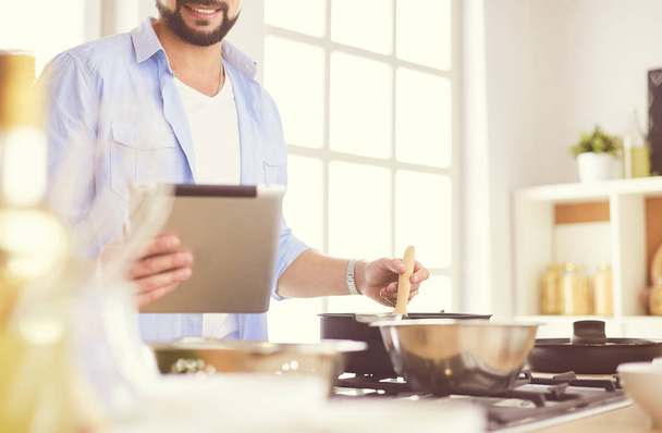 Man following recipe on digital tablet and cooking tasty and healthy food in kitchen at home - 写真・画像
