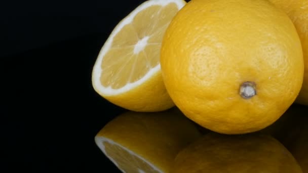 Grote verse gele citroenen op zwarte spiegel oppervlak op een zwarte achtergrond close-up te bekijken. - Video