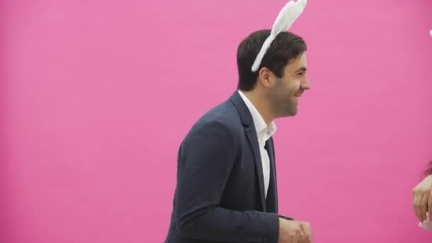 Young sexy couple on pink background. With hackneyed ears on the head. During this, rabbit jumps recreate the movements and looks, after a while go out of the frame. Gently kissed. - 映像、動画