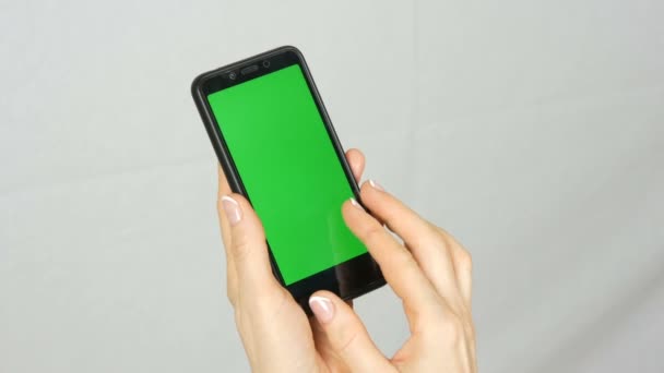 Las manos femeninas pulcras bien arregladas con una hermosa manicura sostienen un teléfono inteligente negro con una pantalla verde o una tecla de cromo sobre fondo blanco en el estudio
 - Imágenes, Vídeo