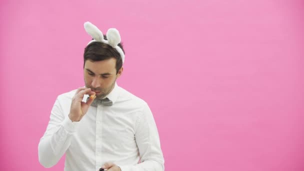 Beautiful boy standing on a pink background. During this dressed in a white shirt. Holding a carrot wants to burn it like a cigar. After a while, he throws carrots to the ground. - Кадры, видео