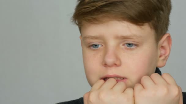 Ritratto di un ragazzo adolescente che si morde le unghie e le dita come se mostrasse ciò che sta vivendo o di cui ha paura su sfondo bianco nello studio. Emozioni e simboli
 - Filmati, video