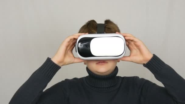 Tiener jongen kijkt in witte virtual reality bril of VR en heeft plezier op een witte achtergrond in de Studio. Toekomst is nu. - Video