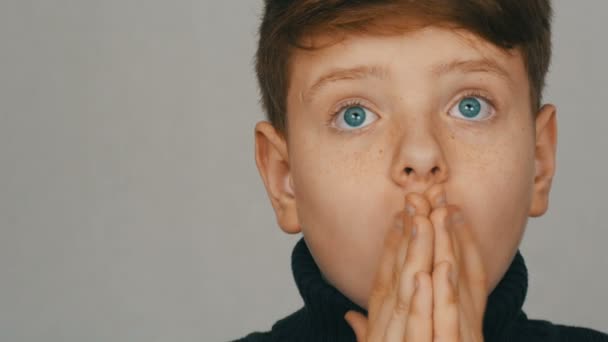 Portré egy szőke és kék szemű tinédzser fiú vicces meglepett előtt a kamera fehér háttérrel. Tinédzserek érzelmei - Felvétel, videó