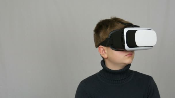 Teenager ragazzo guarda in bianco occhiali di realtà virtuale o VR e si diverte su uno sfondo bianco in studio. Il futuro è ora
. - Filmati, video