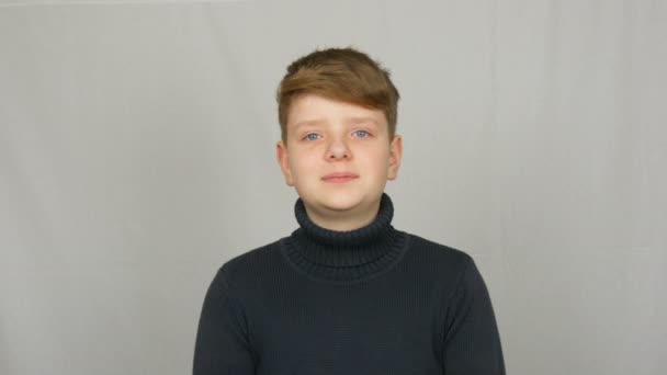 Πορτρέτο ενός όμορφου νεαρού αγοριού με κόκκινα μαλλιά και μπλε μάτια με φακίδες σε ένα πουλόβερ σε λευκό φόντο στο στούντιο - Πλάνα, βίντεο