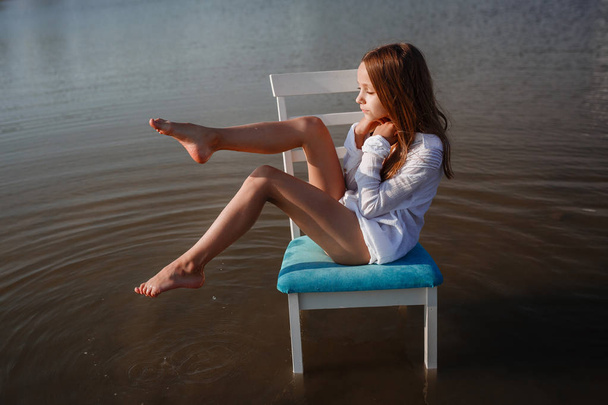 Ένα όμορφο μικρό κορίτσι σε μια καρέκλα στη μέση μιας λίμνης. - Φωτογραφία, εικόνα
