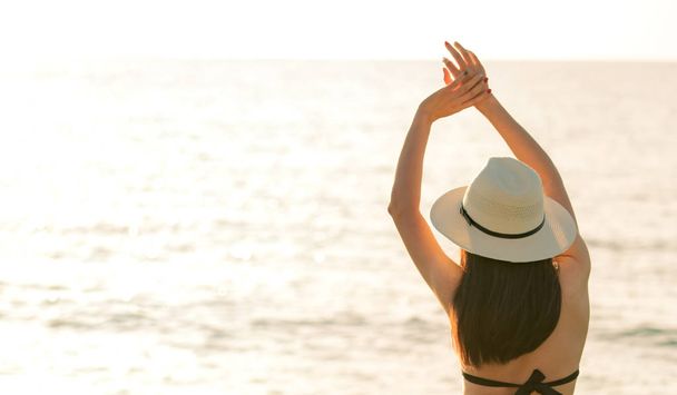 Vue arrière de la jeune femme asiatique heureuse en bikini noir et chapeau de paille se détendre et profiter à la plage paradis tropical au coucher du soleil. Fille dans la mode des vacances d'été. Modèle sexy. Style de vie élégant. Ambiances estivales
. - Photo, image
