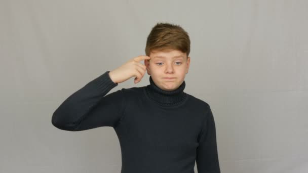 Мальчик-подросток с портретом скручивает палец на виске и укоризненно смотрит на белом фоне в студии. Эмоции подростков
 - Кадры, видео