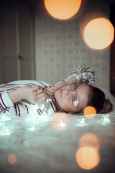 Young woman with fairy lights dreaming in bed - Foto, afbeelding