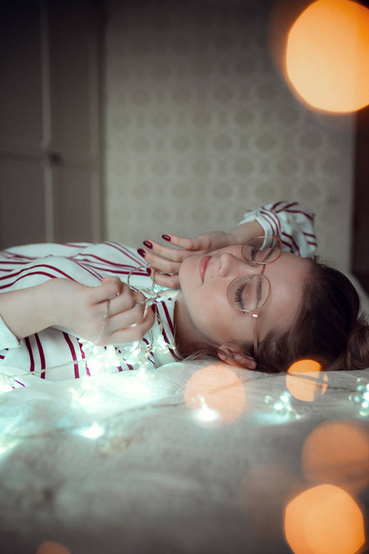 Jeune femme avec des lumières de fées rêvant au lit
 - Photo, image