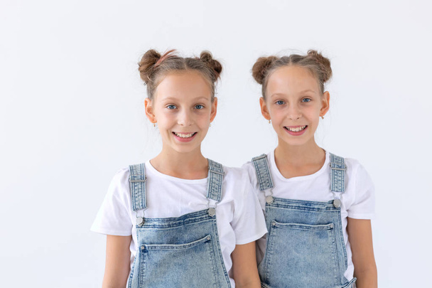 Familien- und Liebeskonzept - zwei lächelnde Zwillingsschwestern, die sich vor weißem Hintergrund umarmen - Foto, Bild