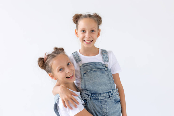 Concepto de familia y amor: dos hermanas gemelas sonrientes abrazándose sobre un fondo blanco
 - Foto, imagen