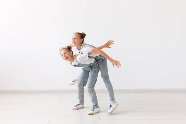 people, children and family concept - little girl carrying her twin sister piggyback on white background - Photo, Image