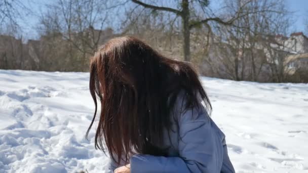 attraktive Frau mit blauer verspiegelter Sonnenbrille und glatten dunklen Haaren, die morgens bei sonnigem, aber kaltem Wetter im Park Schneebälle spielt. Konzept für Winterspiele - Filmmaterial, Video