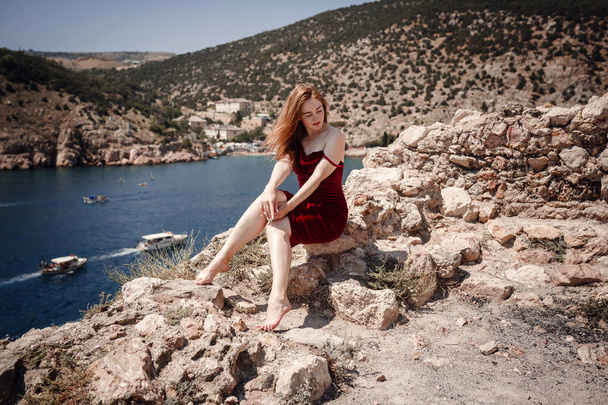 美しい赤毛の女性が岩の上に座っている - 写真・画像