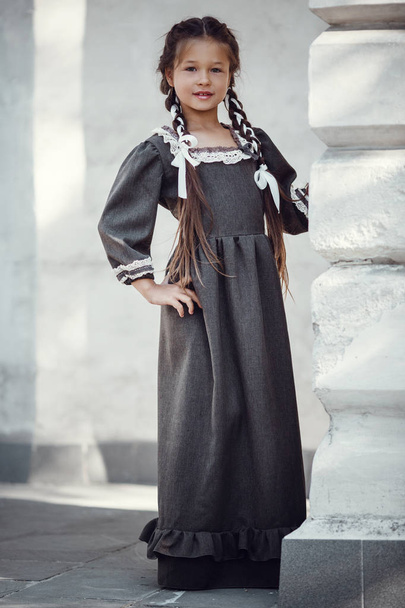 Krásná holčička ve starých šatech na pozadí architektury historického centra - Fotografie, Obrázek