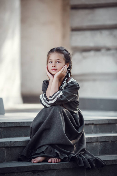 Όμορφο μικρό κορίτσι σε ένα παλιό φόρεμα στο φόντο της αρχιτεκτονικής του ιστορικού κέντρου - Φωτογραφία, εικόνα