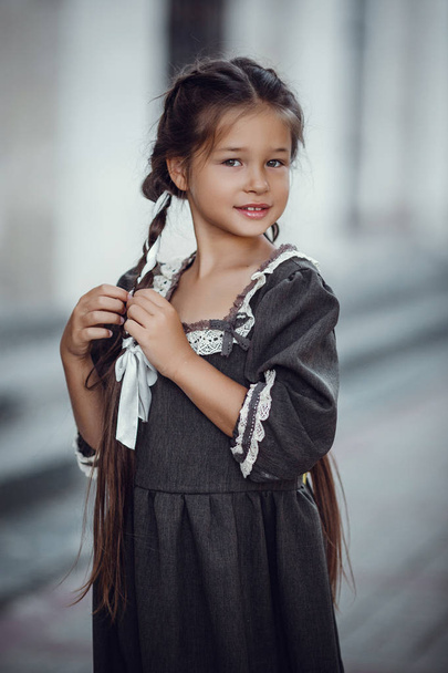 Όμορφο μικρό κορίτσι σε ένα παλιό φόρεμα στο φόντο της αρχιτεκτονικής του ιστορικού κέντρου - Φωτογραφία, εικόνα